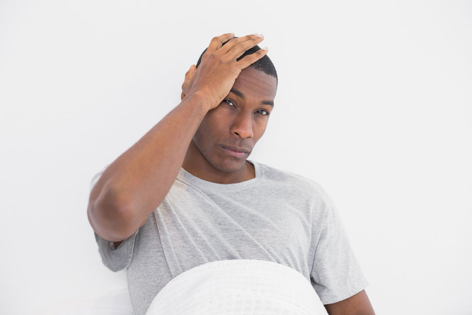 Portrait of a young Afro man suffering from headache in bed at home